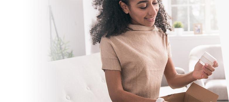 Young woman removes sample jar of cream from a marketing mail parcel.